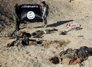 ATTENTION EDITORS - VISUAL COVERAGE OF SCENES OF INJURY OR DEATH Iraqi security forces hold an Islamist State flag near the bodies of dead members of the Islamic State in the outskirt of Ramadi December 23, 2014. Picture taken December 23, 2014. REUTERS/Stringer (IRAQ - Tags: CONFLICT TPX IMAGES OF THE DAY) TEMPLATE OUT - RTR4JC85